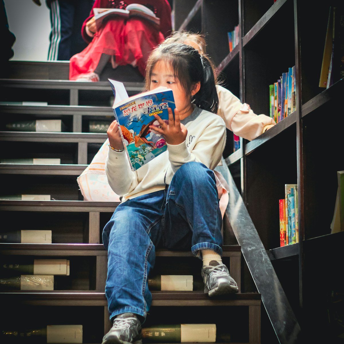 Petite fille assise dans une bibliothèque en train de lire un livre